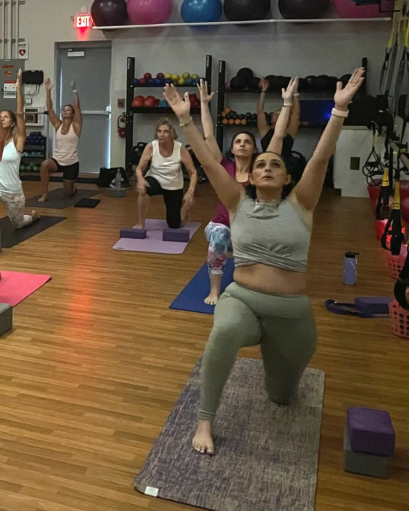 A yoga class holding a crescent lunge, arms raised